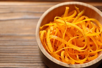 Photo of Fresh orange zest in bowl on wooden table, closeup. Space for text