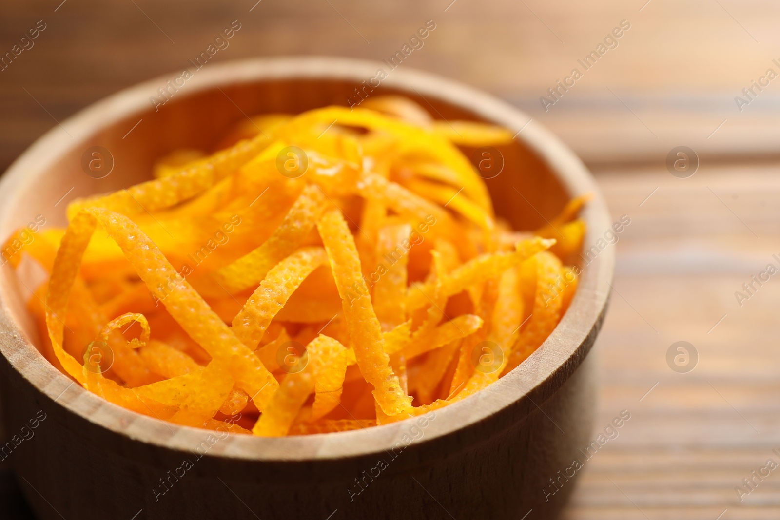 Photo of Fresh orange zest in bowl on wooden table, closeup