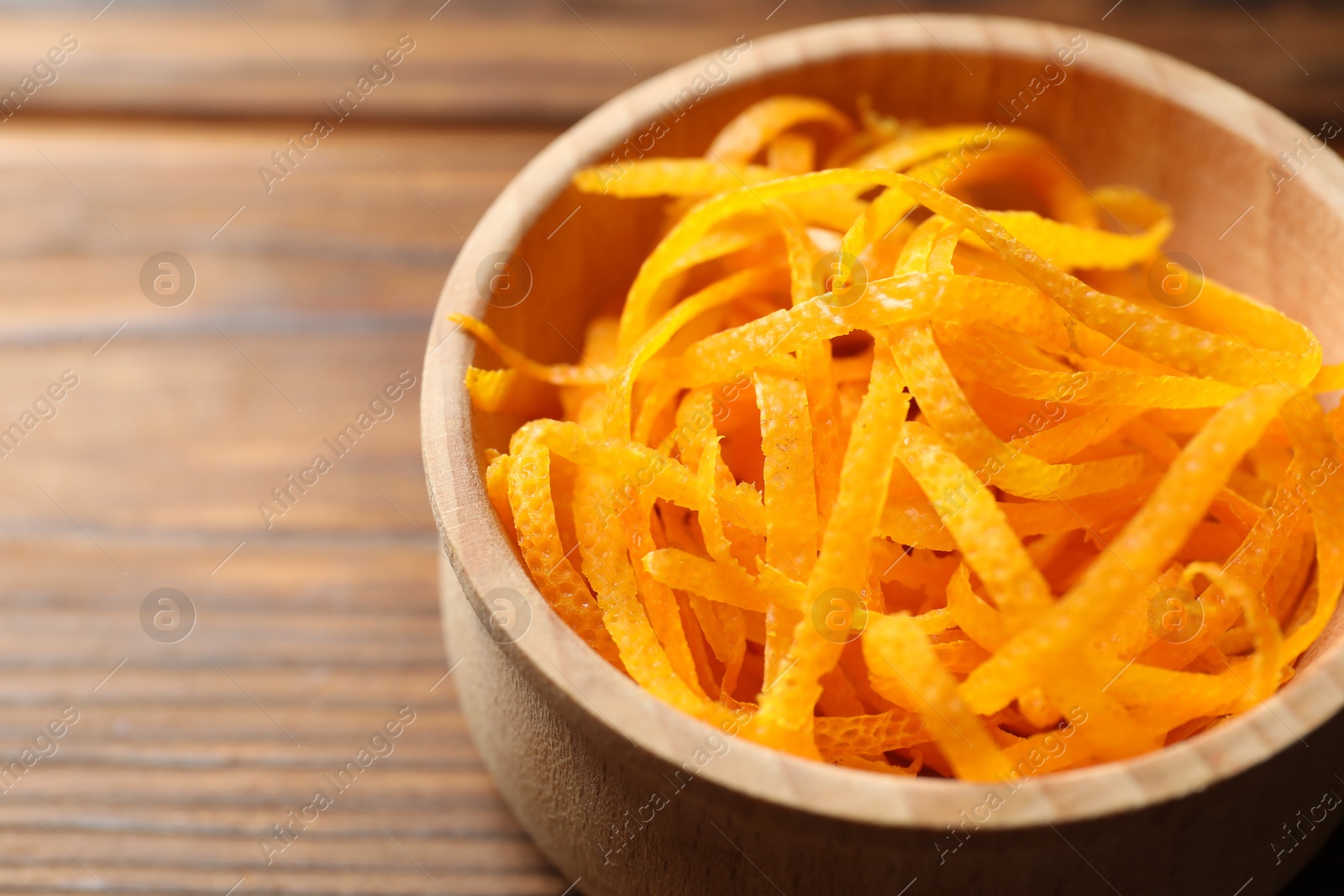 Photo of Fresh orange zest in bowl on wooden table, closeup