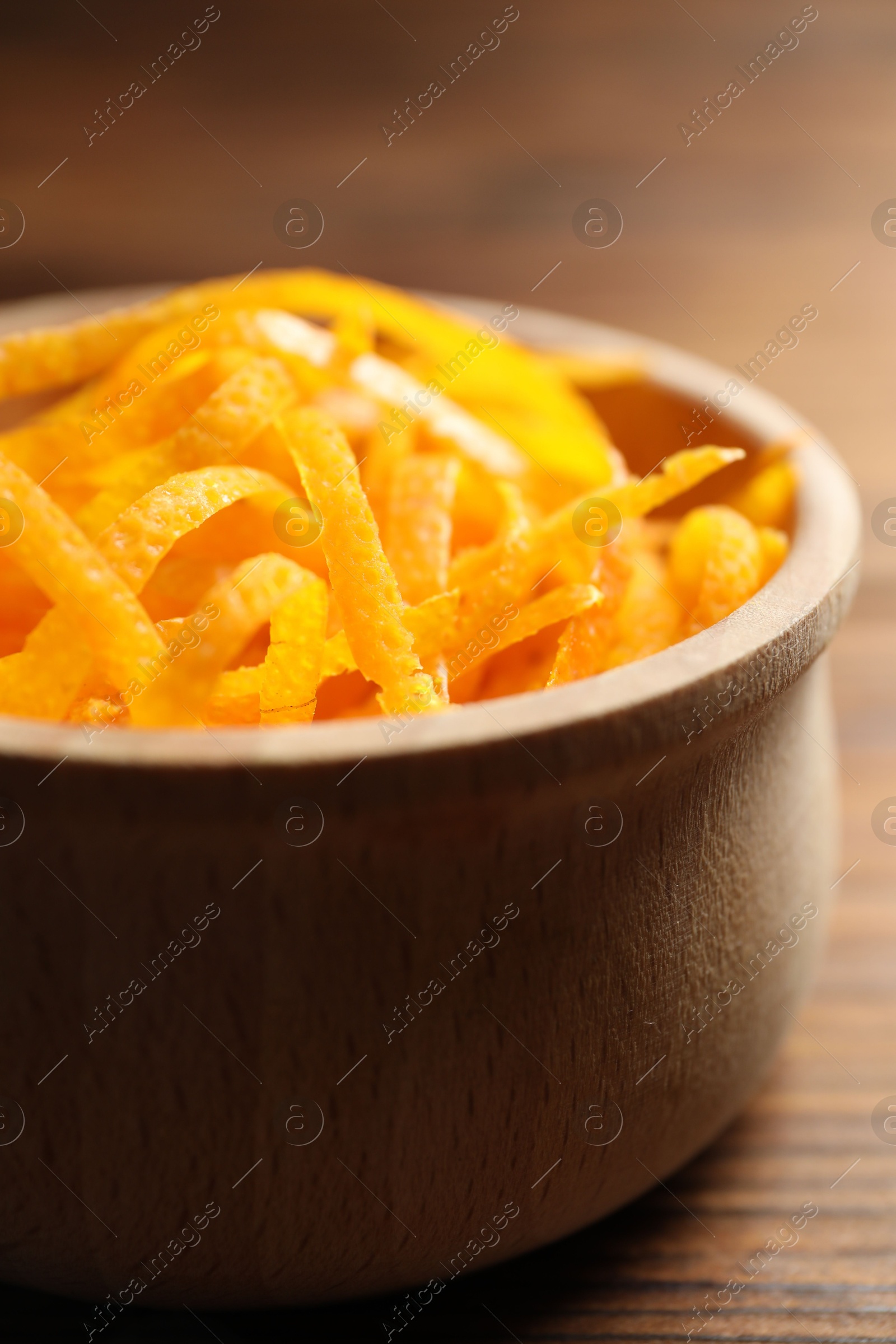 Photo of Fresh orange zest in bowl on wooden table, closeup