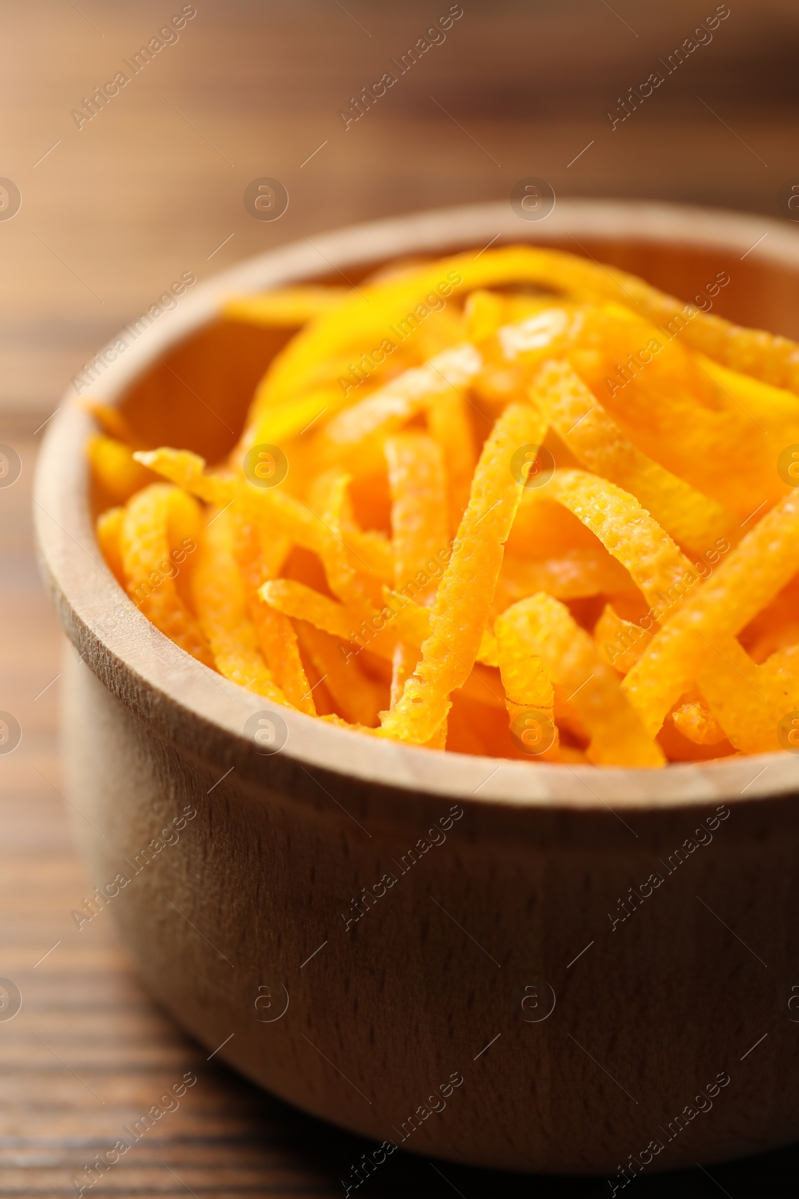 Photo of Fresh orange zest in bowl on wooden table, closeup