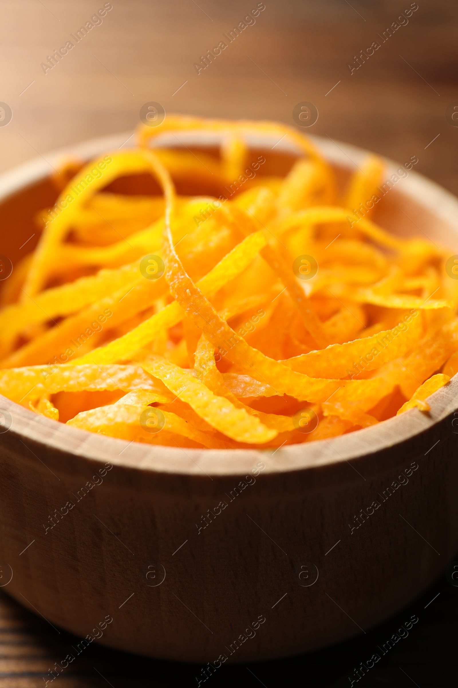 Photo of Fresh orange zest in bowl on wooden table, closeup