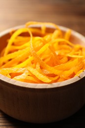 Photo of Fresh orange zest in bowl on wooden table, closeup