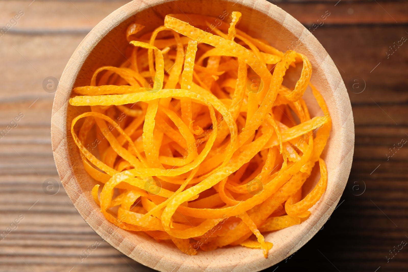 Photo of Fresh orange zest in bowl on wooden table, top view