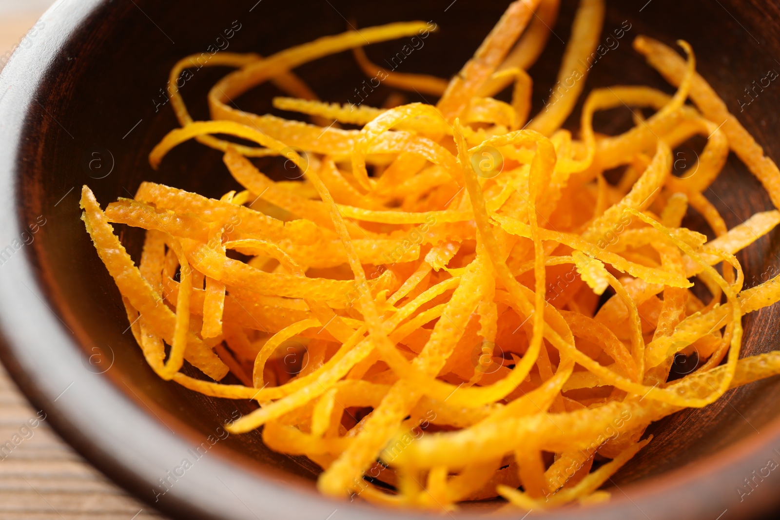 Photo of Fresh orange zest in bowl on wooden table, closeup