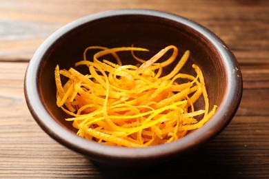 Photo of Fresh orange zest in bowl on wooden table, closeup