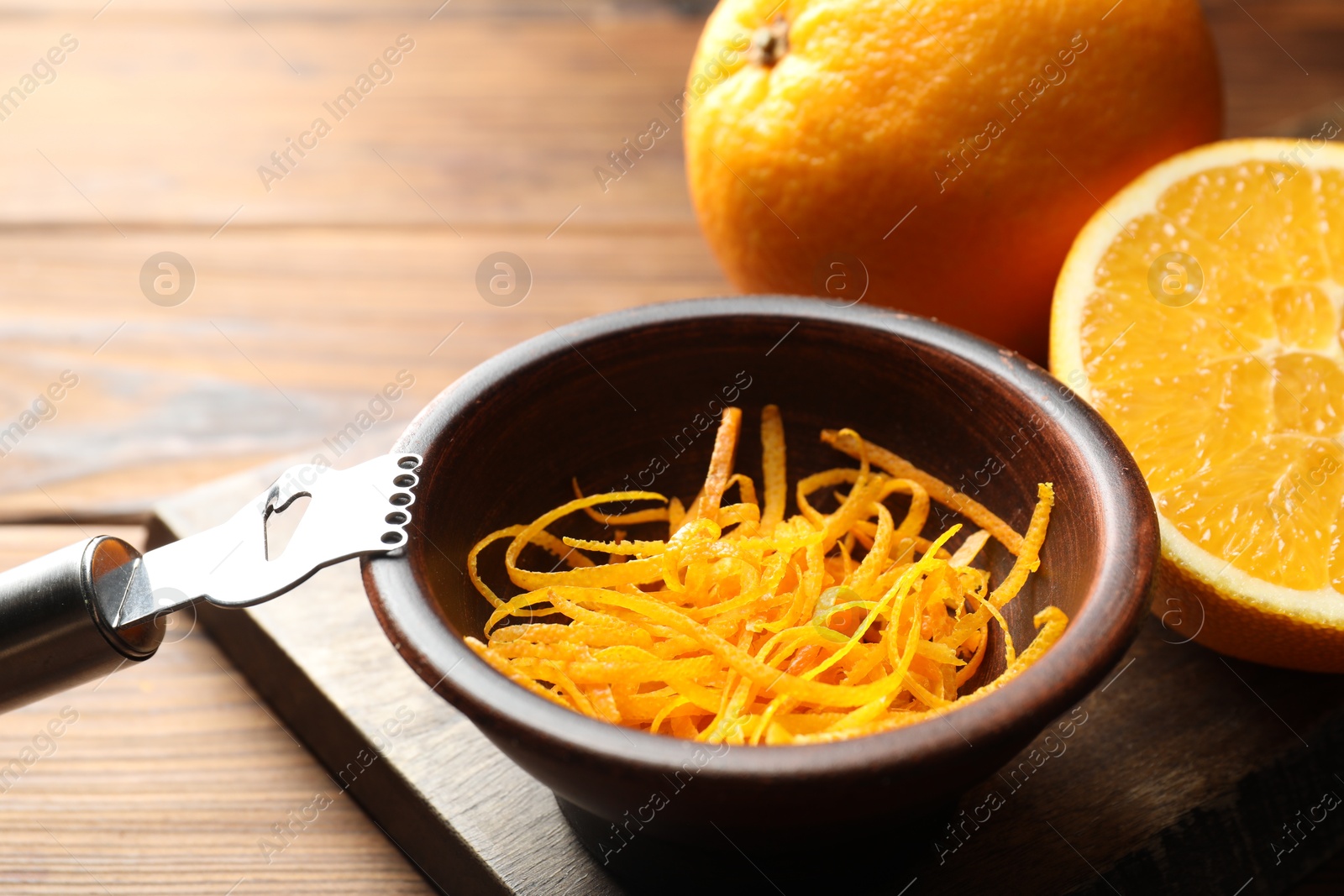 Photo of Orange zest, zester tool and fresh fruits on wooden table, closeup