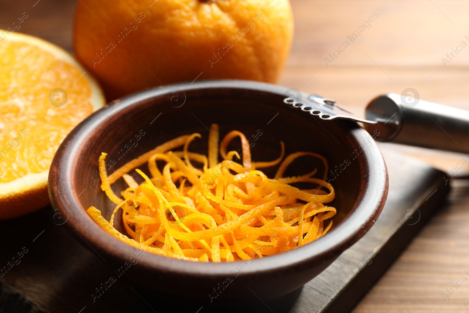 Photo of Orange zest, zester tool and fresh fruits on wooden table, closeup