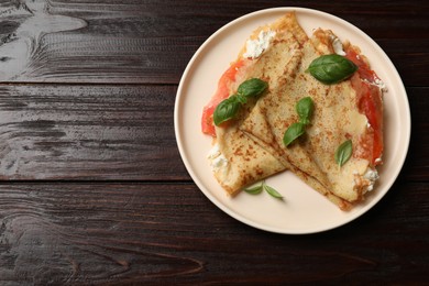 Photo of Delicious crepes with salmon, cream cheese and basil on wooden table, top view. Space for text