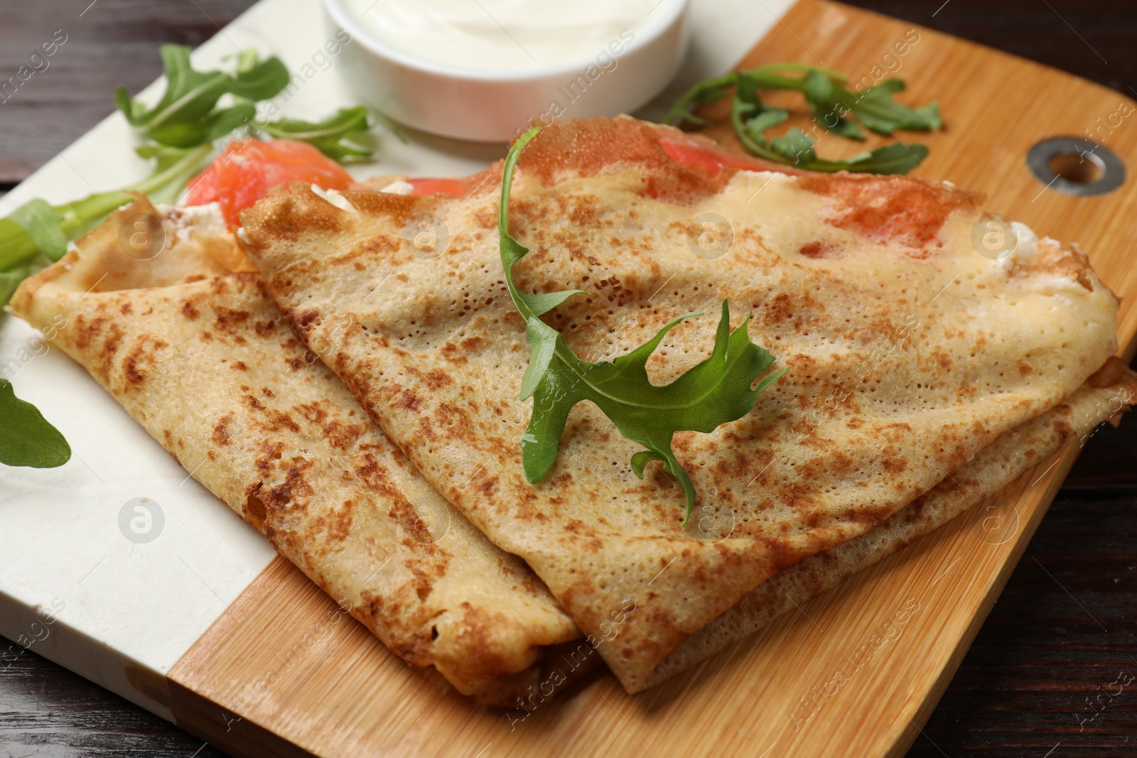 Photo of Delicious crepes with salmon, cream cheese and arugula on wooden table, closeup