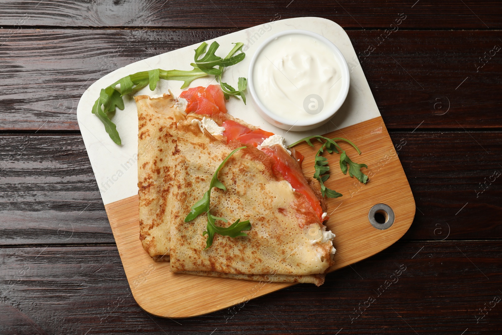 Photo of Delicious crepes with salmon, cream cheese and arugula on wooden table, top view