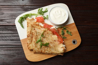 Photo of Delicious crepes with salmon, cream cheese and arugula on wooden table, top view