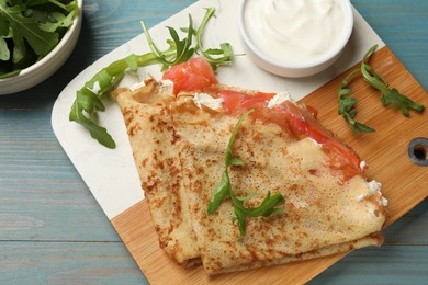 Photo of Delicious crepes with salmon, cream cheese and arugula on blue wooden table, closeup