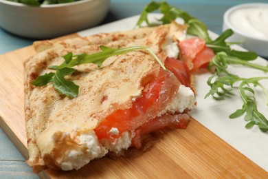 Photo of Delicious crepes with salmon, cream cheese and arugula on blue wooden table, closeup