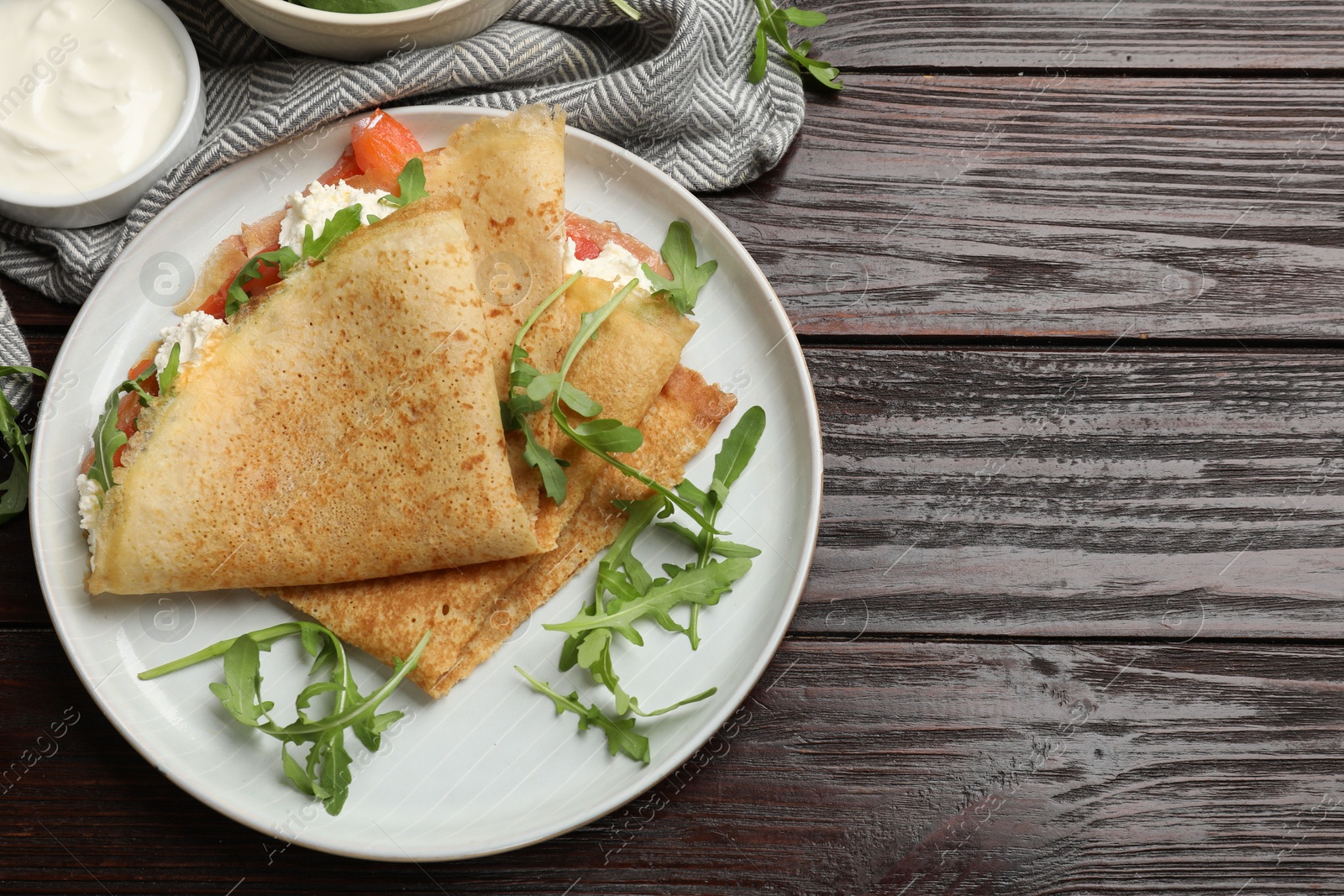 Photo of Delicious crepes with salmon, cream cheese and arugula on wooden table, flat lay. Space for text