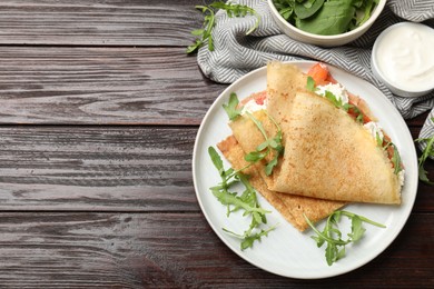 Photo of Delicious crepes with salmon, cream cheese and arugula on wooden table, flat lay. Space for text