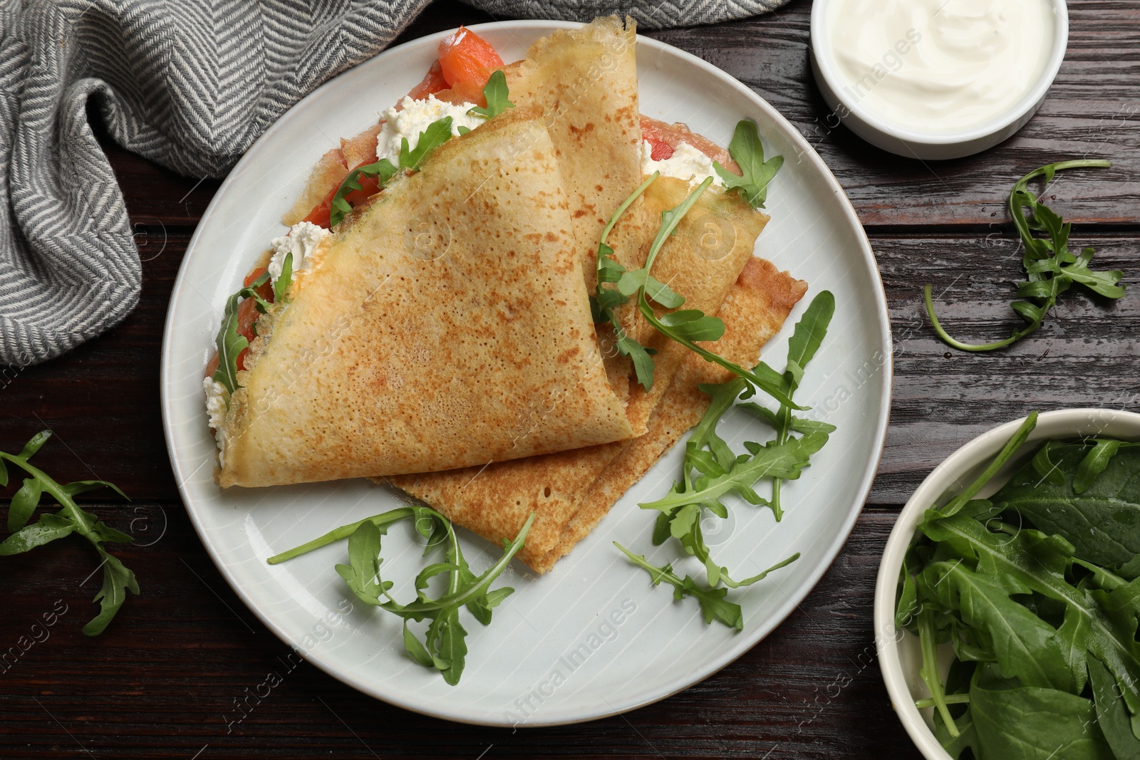 Photo of Delicious crepes with salmon, cream cheese and arugula on wooden table, flat lay