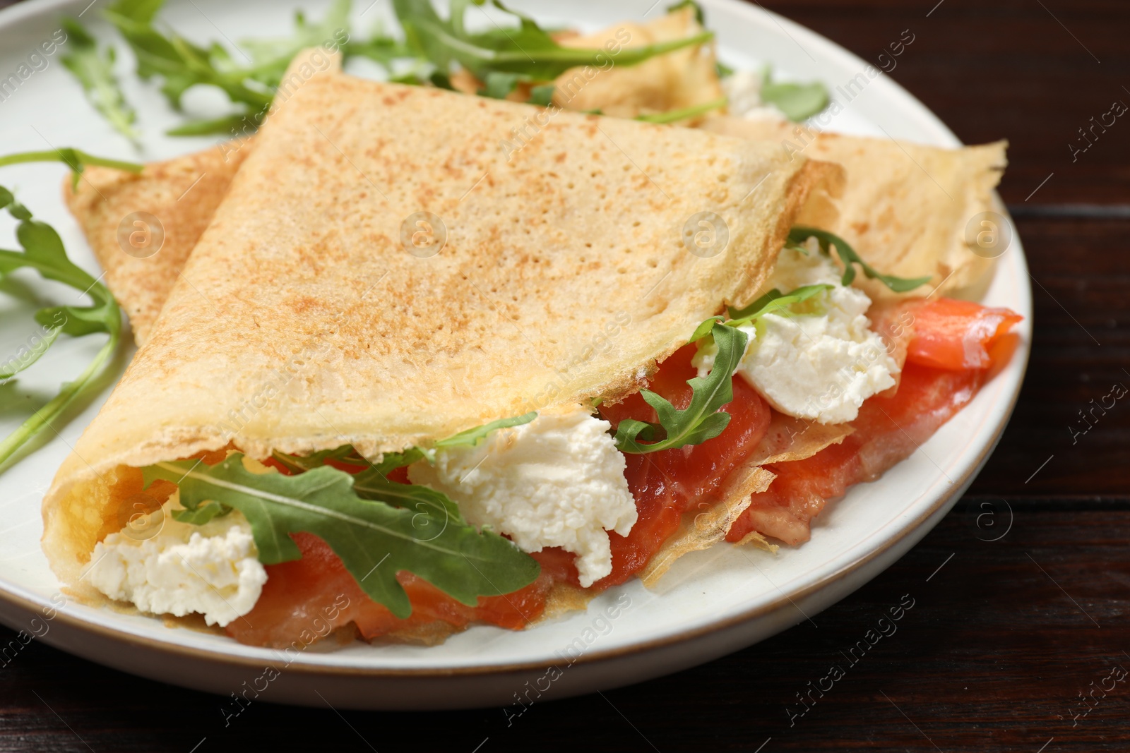 Photo of Delicious crepes with salmon, cream cheese and arugula on wooden table, closeup