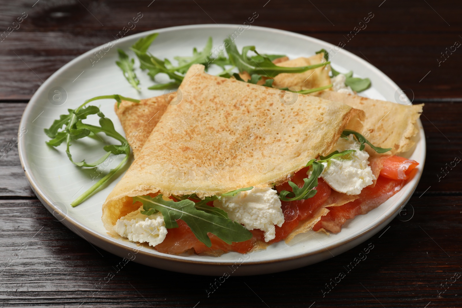 Photo of Delicious crepes with salmon, cream cheese and arugula on wooden table, closeup