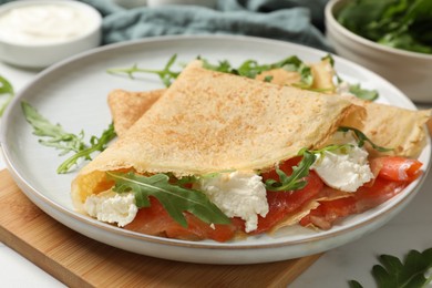 Photo of Delicious crepes with salmon, cream cheese and arugula on white table, closeup