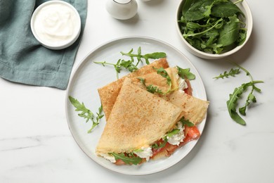 Photo of Delicious crepes with salmon, cream cheese and arugula on white marble table, flat lay