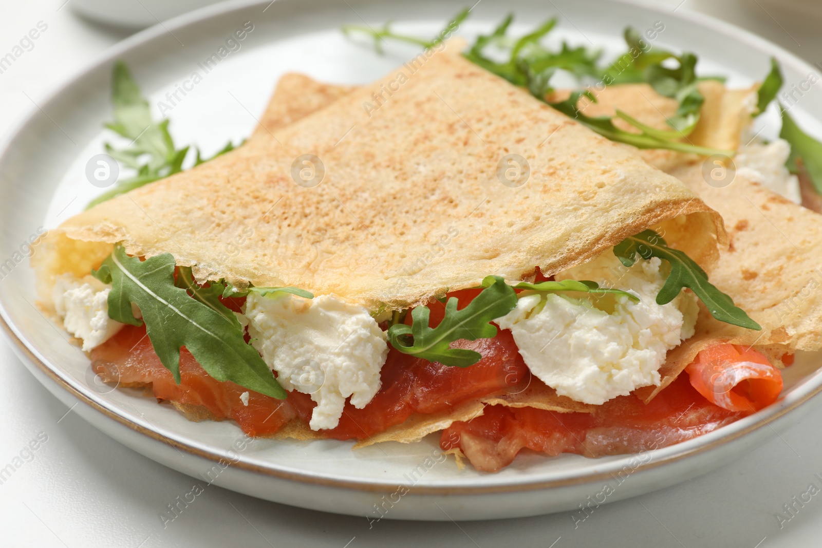 Photo of Delicious crepes with salmon, cream cheese and arugula on white table, closeup