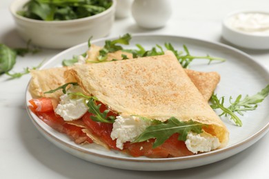 Photo of Delicious crepes with salmon, cream cheese and arugula on white table, closeup