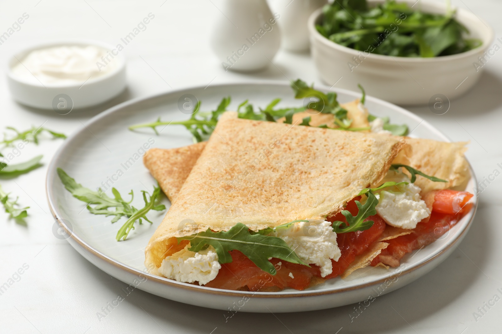 Photo of Delicious crepes with salmon, cream cheese and arugula on white table, closeup