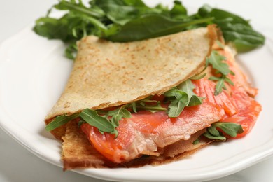 Photo of Delicious crepes with salmon and arugula on white table, closeup