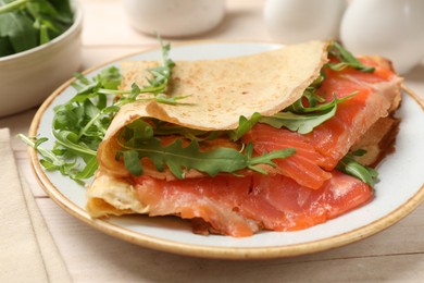 Photo of Delicious crepes with salmon and arugula on white wooden table, closeup