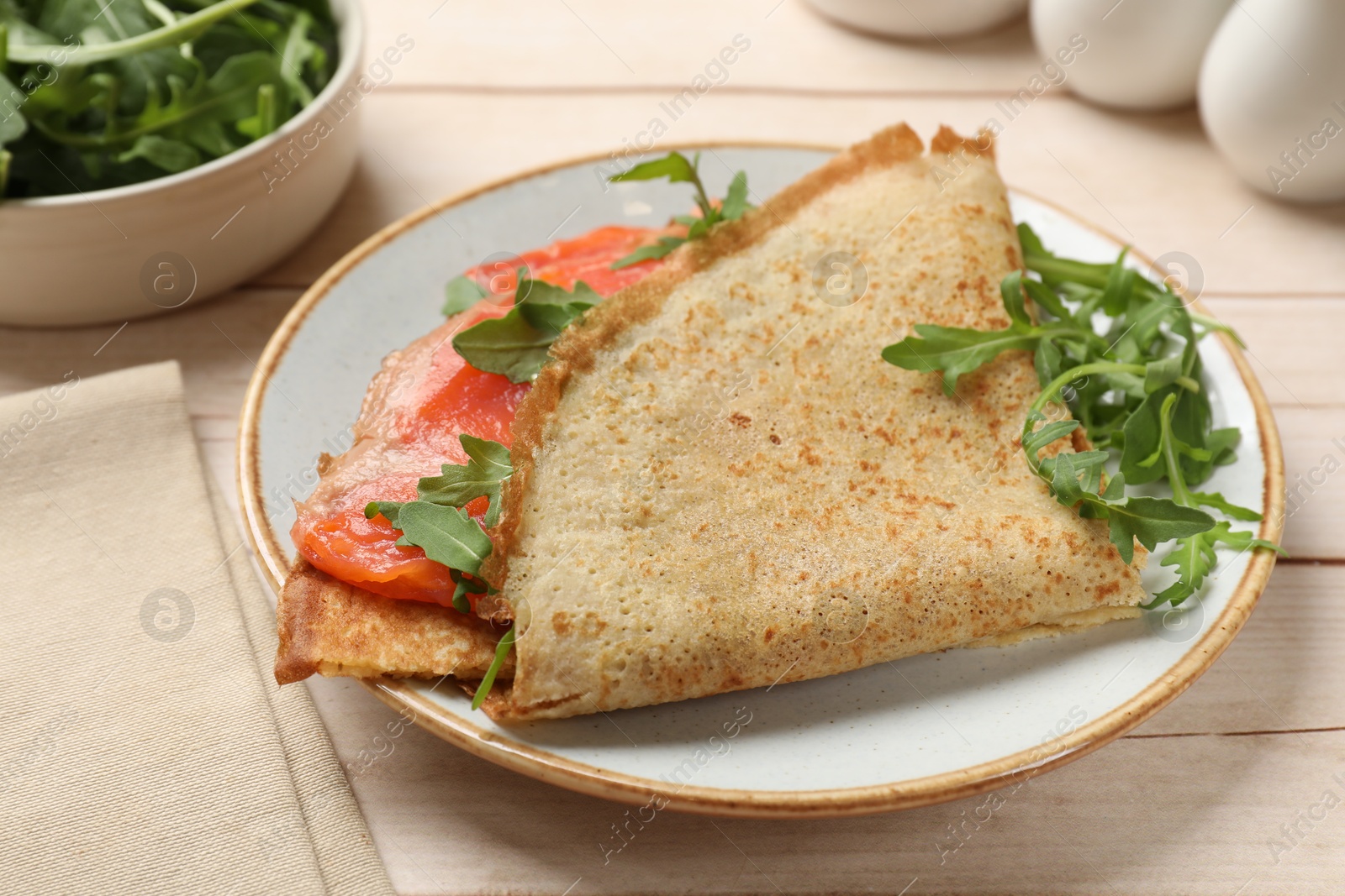 Photo of Delicious crepes with salmon and arugula on white wooden table, closeup