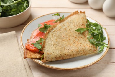 Photo of Delicious crepes with salmon and arugula on white wooden table, closeup