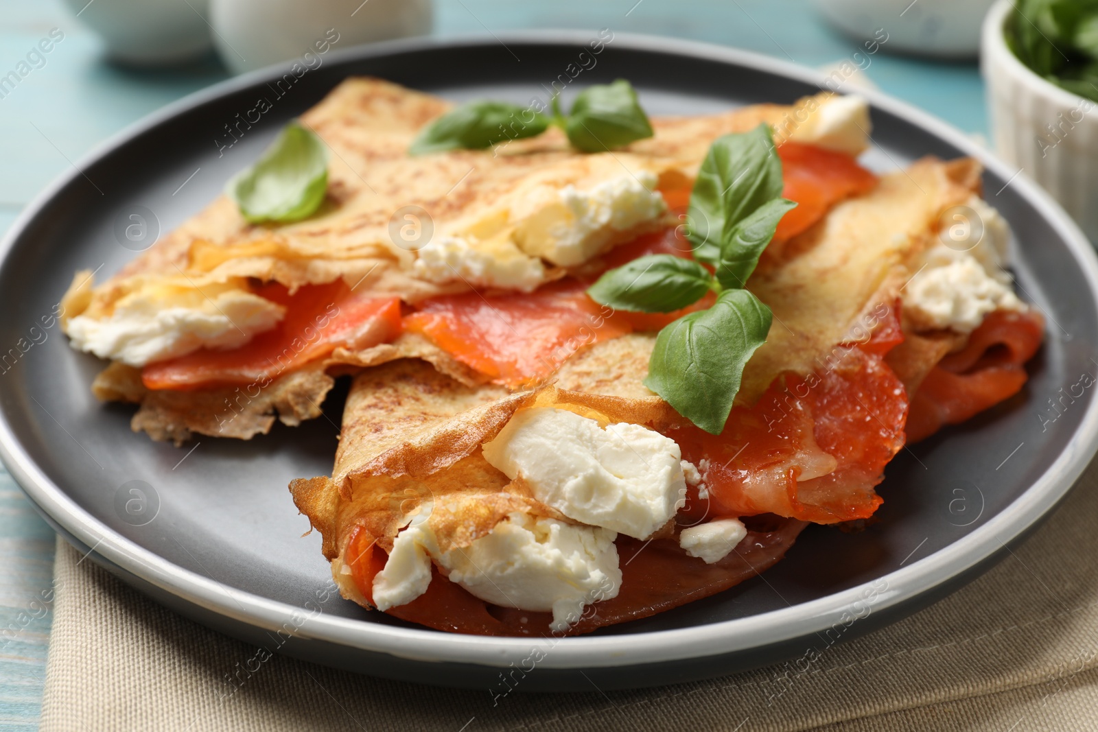 Photo of Delicious crepes with salmon, cream cheese and basil on table, closeup