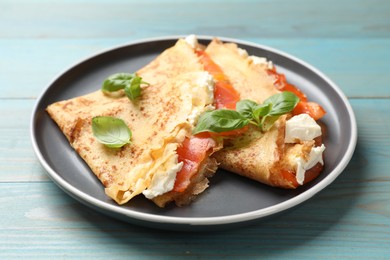 Photo of Delicious crepes with salmon, cream cheese and basil on light blue wooden table, closeup