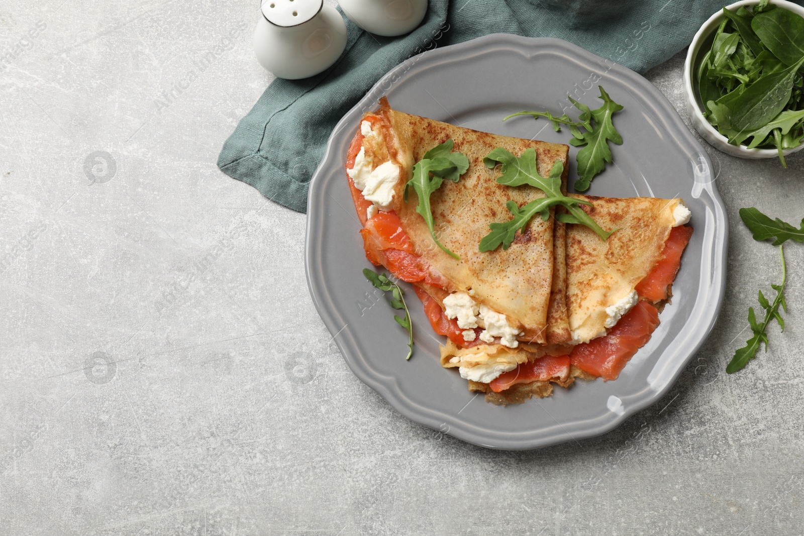 Photo of Delicious crepes with salmon, cream cheese and arugula on grey table, flat lay. Space for text