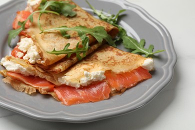 Photo of Delicious crepes with salmon, cream cheese and arugula on white table, closeup