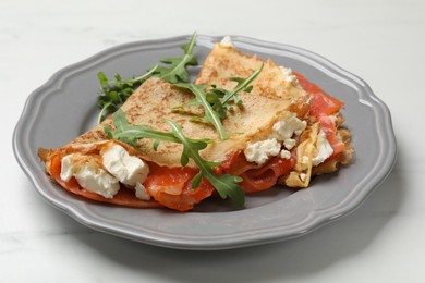 Photo of Delicious crepes with salmon, cream cheese and arugula on white marble table, closeup