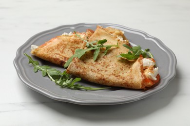 Photo of Delicious crepes with salmon, cream cheese and arugula on white marble table, closeup