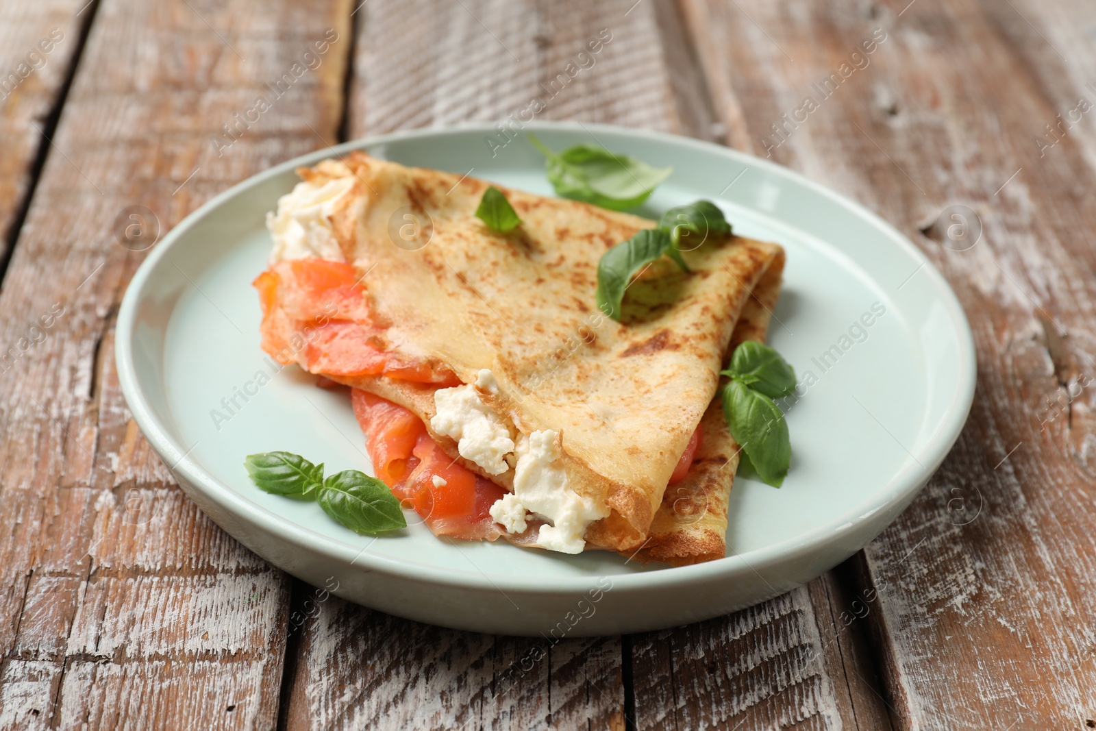 Photo of Delicious crepe with salmon, cream cheese and basil on wooden table, closeup