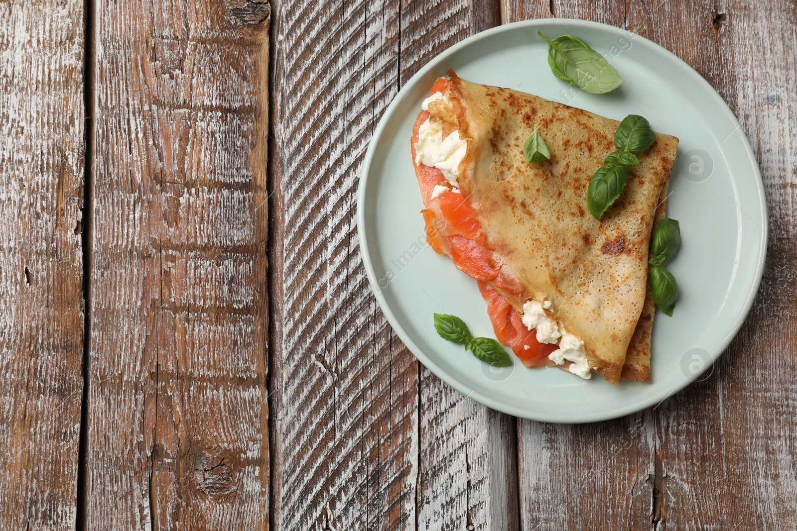 Photo of Delicious crepe with salmon, cream cheese and basil on wooden table, top view. Space for text