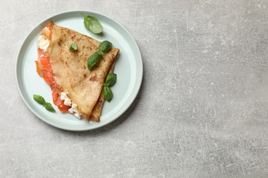 Photo of Delicious crepe with salmon, cream cheese and basil on grey table, top view. Space for text