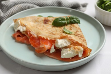 Photo of Delicious crepe with salmon, cream cheese and basil on white table, closeup