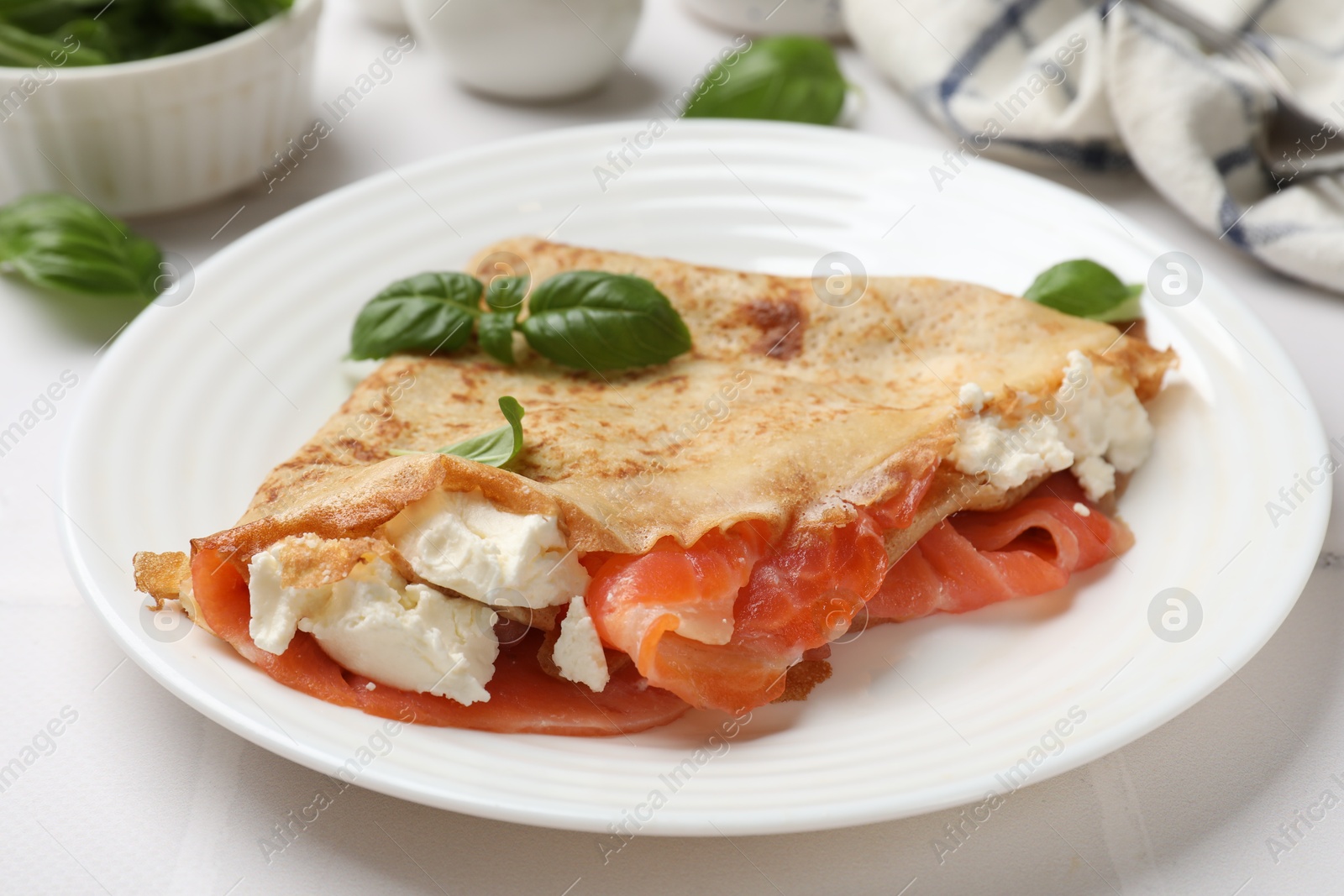 Photo of Delicious crepe with salmon, cream cheese and basil on white table, closeup