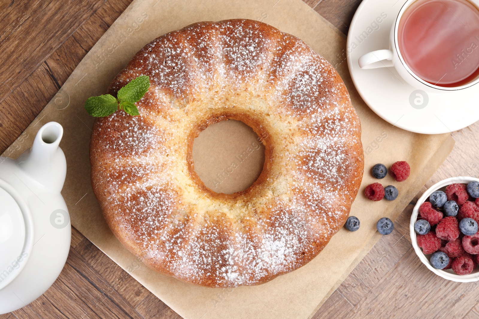 Photo of Freshly baked sponge cake, tea and berries on wooden table, top view