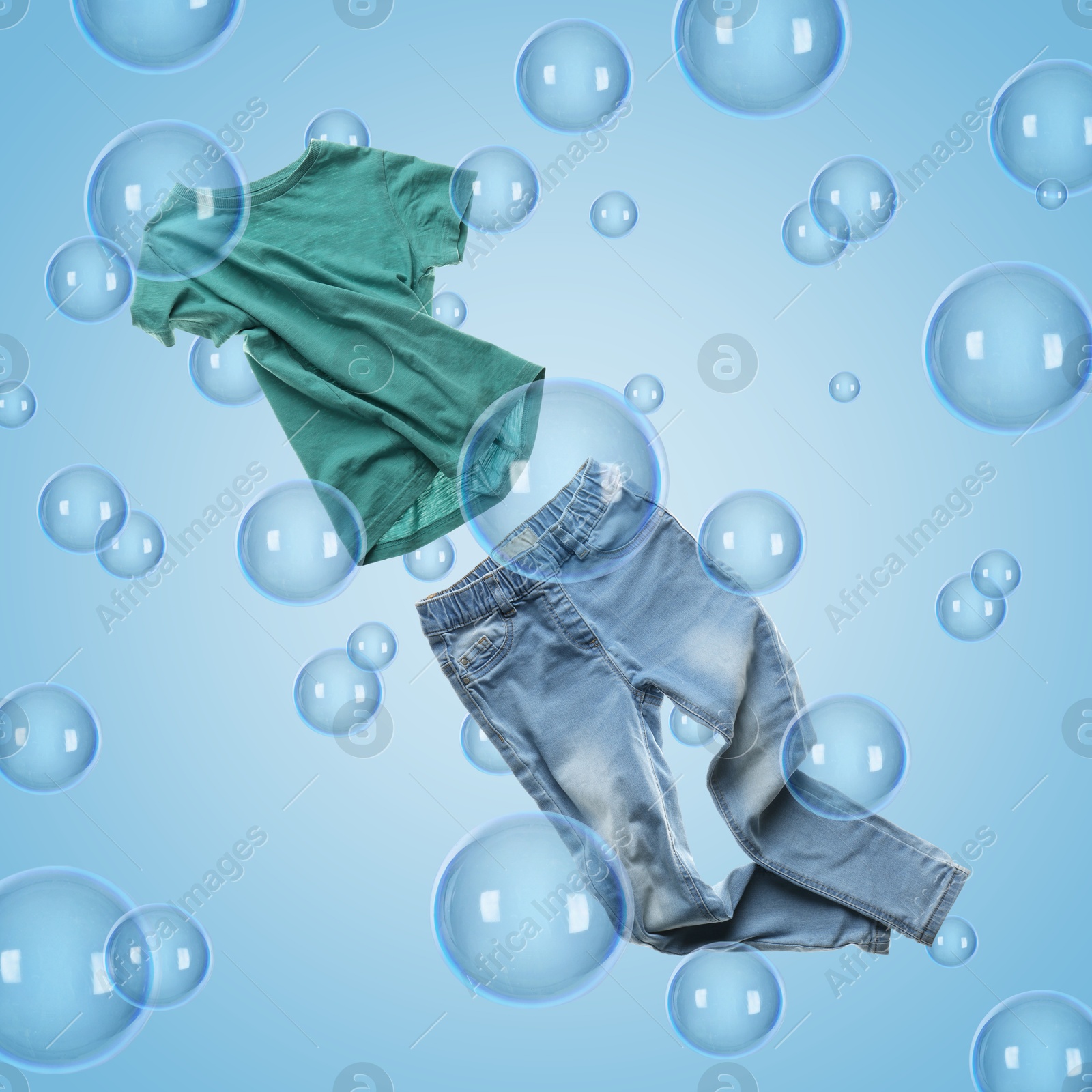 Image of T-shirt and jeans flying among soap bubbles on light blue background. Laundry day