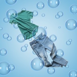 Image of T-shirt and jeans flying among soap bubbles on light blue background. Laundry day