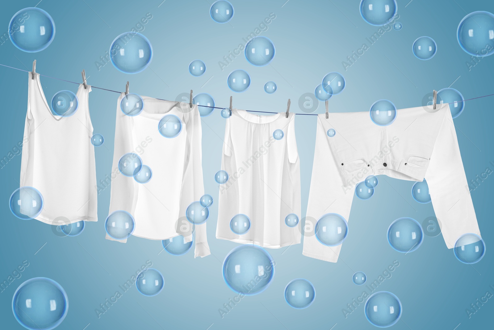 Image of Laundry hanging on clothes rope among floating soap bubbles on light blue background