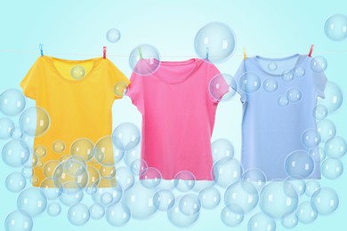 Image of Laundry hanging on clothes rope among floating soap bubbles on light blue background