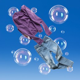 Image of Sweater and jeans flying among soap bubbles on blue background. Laundry day