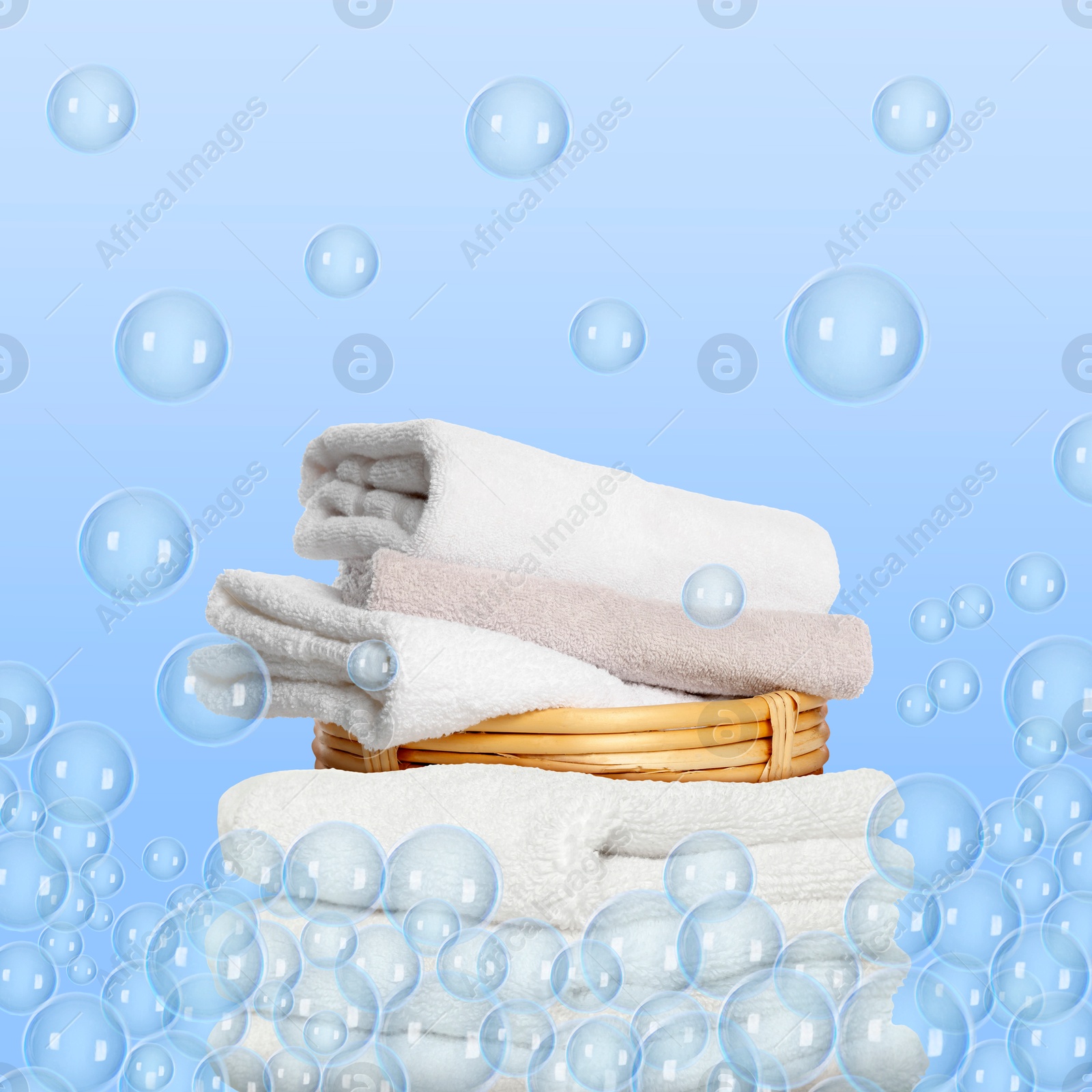 Image of Stacked laundry and floating soap bubbles on light blue background